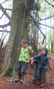 3 young children swinging on a rope swing in the woods